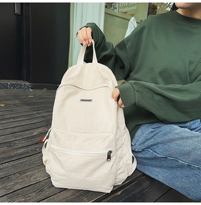 Detail of a minimalist cream canvas backpack featuring a front zipper pocket and logo patch