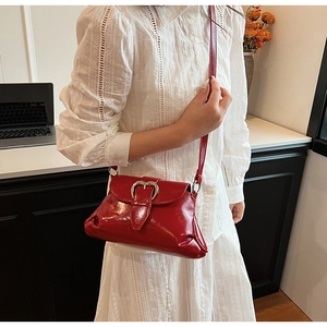 Detail of red glossy saddle bag with a large silver heart buckle and pleated texture