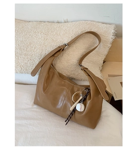 Detail of a brown Hobo shoulder bag with a baseball charm on soft bedding