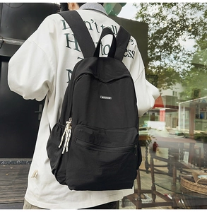 Outdoor back view of a black canvas backpack with woven zipper pulls and brand logo