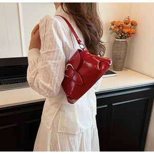 Glossy red patent leather saddle bag with large metal buckle on a white dress model