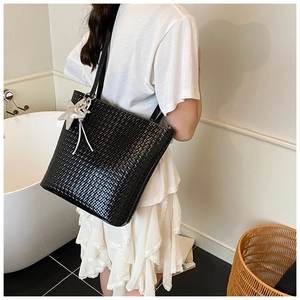 Detail of black woven bucket bag with silver star pendant and sleek faux leather texture