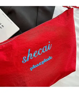 Detail of red oversized dumpling bag featuring blue text print and pleated nylon fabric texture
