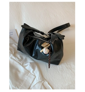 Close-up of black glossy leather tote bag with unique baseball charm on white bedding