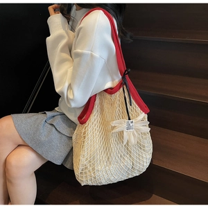 Detail of knit mesh shoulder bag with red handles and white floral pendant detail