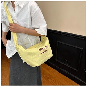 Detail of yellow nylon pleated dumpling bag with red lettering on a wide shoulder strap