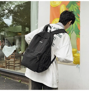 Side view of black nylon backpack featuring a zippered front pocket and side bottle pouch