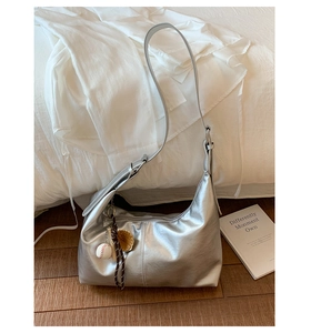 Detailed shot of silver crescent tote bag with baseball charm on wooden floor