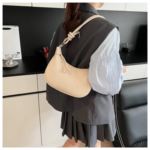 Detail of pleated beige hobo bag with knotted shoulder strap on a model indoors