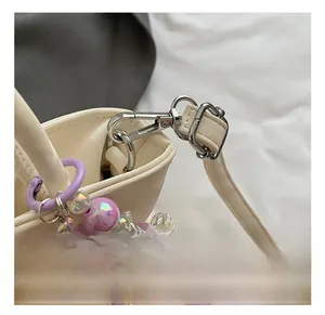 Detail of silver metal swivel hook and purple bead charm on off-white leather handbag
