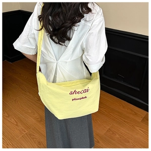 Detail of light yellow crescent shoulder bag with artistic text and adjustable wide strap