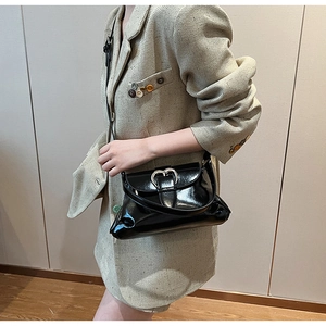 Detail of black patent leather saddle bag featuring a silver heart buckle on a model