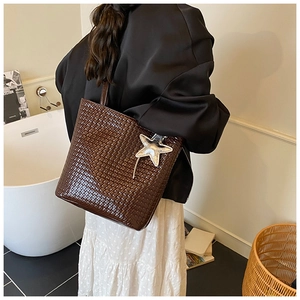Detail view of dark brown woven leather tote with a silver star pendant and shoulder strap
