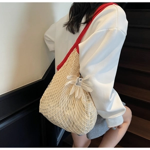Detail of a white crochet net bag with a bold red shoulder strap and floral charm