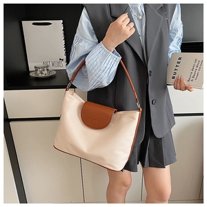 Detail view of cream crossbody bag with brown leather trim worn by a model in lifestyle setting