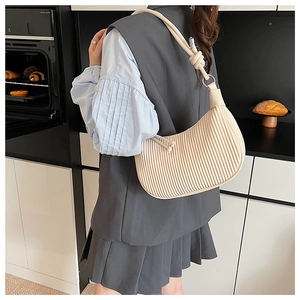 Detail view of cream pleated underarm bag with knotted strap on a lifestyle model