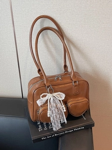 Brown glossy leather bowling bag with pearl bow charm on vintage art book display