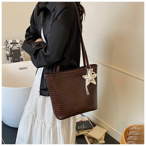 Close-up of a large coffee brown woven tote bag featuring a silver star pendant