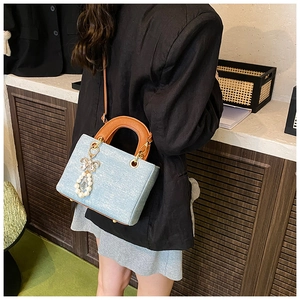 Detail of light blue square tote bag with distinctive circular handle and pearl charm