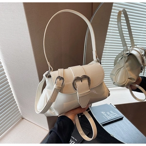 Detail view of cream patent leather saddle bag featuring a silver heart-shaped metal buckle