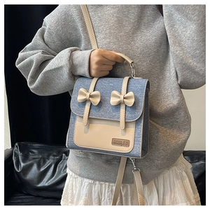 Detail of blue denim and beige leather patchwork bag with bows and brand logo