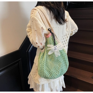 Close-up of green mesh knit tote bag with floral charm and drawstring closure details