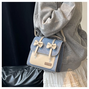 Detail view of denim crossbody bag with white PU leather trim and bow decorations