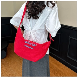 Close-up of bright red crescent bag featuring blue embroidery and pleated canvas texture