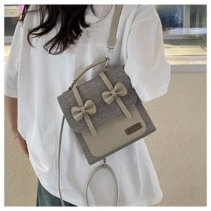 Detail of grey textured fabric crossbody bag featuring cute beige 3D bows and leather trim