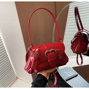 Detail of red patent leather saddle bag featuring a polished silver heart buckle