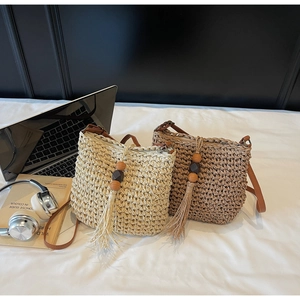 Dettaglio della borsa a secchiello in paglia intrecciata con nappe di legno e tracolla in pelle
