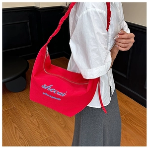 Macro detail of red dumpling bag featuring blue logo embroidery and pleated strap texture