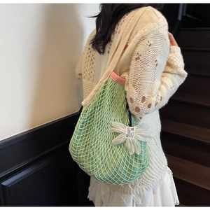 Detail showing light green mesh beach bag with large white daisy charm and wide strap