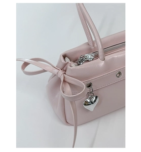 Detail of pink faux leather handbag showing side leather bow and silver heart pendant