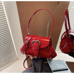 Detail of red patent leather saddle bag featuring a silver heart-shaped metal buckle