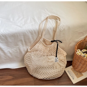 Detail of cream crochet tote bag with black ribbon and floral charm on a white bed