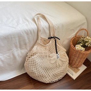 Detail of cream woven mesh beach bag with decorative fabric flower and black ribbon bow
