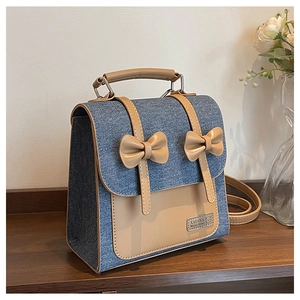 Detail shot of the blue denim and khaki faux leather bag featuring a bow and metal logo