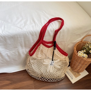Detail of large mesh beach bag featuring red straps and a white daisy charm decoration