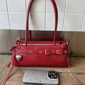 Detail of red leather baguette bag with bow accent and silver heart pendant charm
