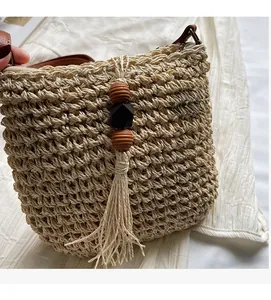 Dettaglio borsa a secchiello in paglia con nappa decorativa di perle e tracolla in pelle