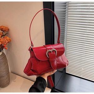 Close-up of red glossy saddle bag featuring a bold heart-shaped metal buckle and flap cover