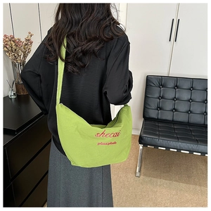 Detail of neon green canvas crossbody bag with red embroidery on a half-moon shaped body