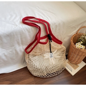 Detailed close-up of woven mesh tote with contrast red handles and floral charm decoration