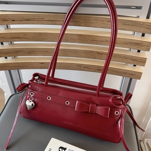 Macro shot of red glossy leather baguette bag with silver heart charm and bow detail