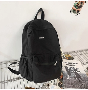 Detail of a black canvas backpack with front zipper pocket and side mesh storage pockets