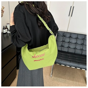 Detail of lime green shoulder bag featuring red letter embroidery and ruched strap design