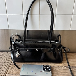 Detail of black glossy shoulder bag with bow, metal grommets and silver heart charm