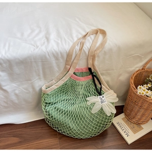 Close-up of green knit mesh tote bag featuring a 3D white flower and internal liner