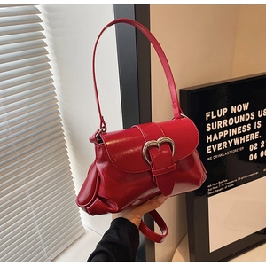 Close-up of red patent leather saddle bag with heart metal buckle and single shoulder strap